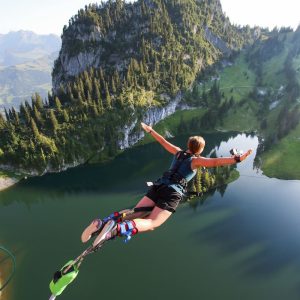 Person jumping off a platform for a bungy jump at Stockhorn, with scenic Swiss lakes and mountains below.