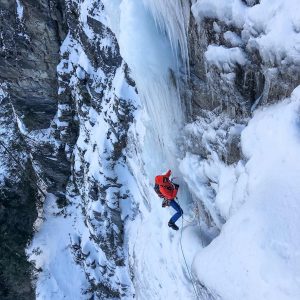 Person ice climbing on a steep, frozen wall in the Swiss Alps, surrounded by snow-covered rocks.