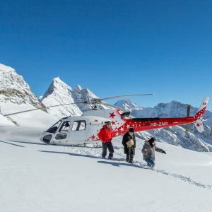Group of people stepping out of a helicopter onto a snow-covered mountain during a scenic flight in the Swiss Alps.