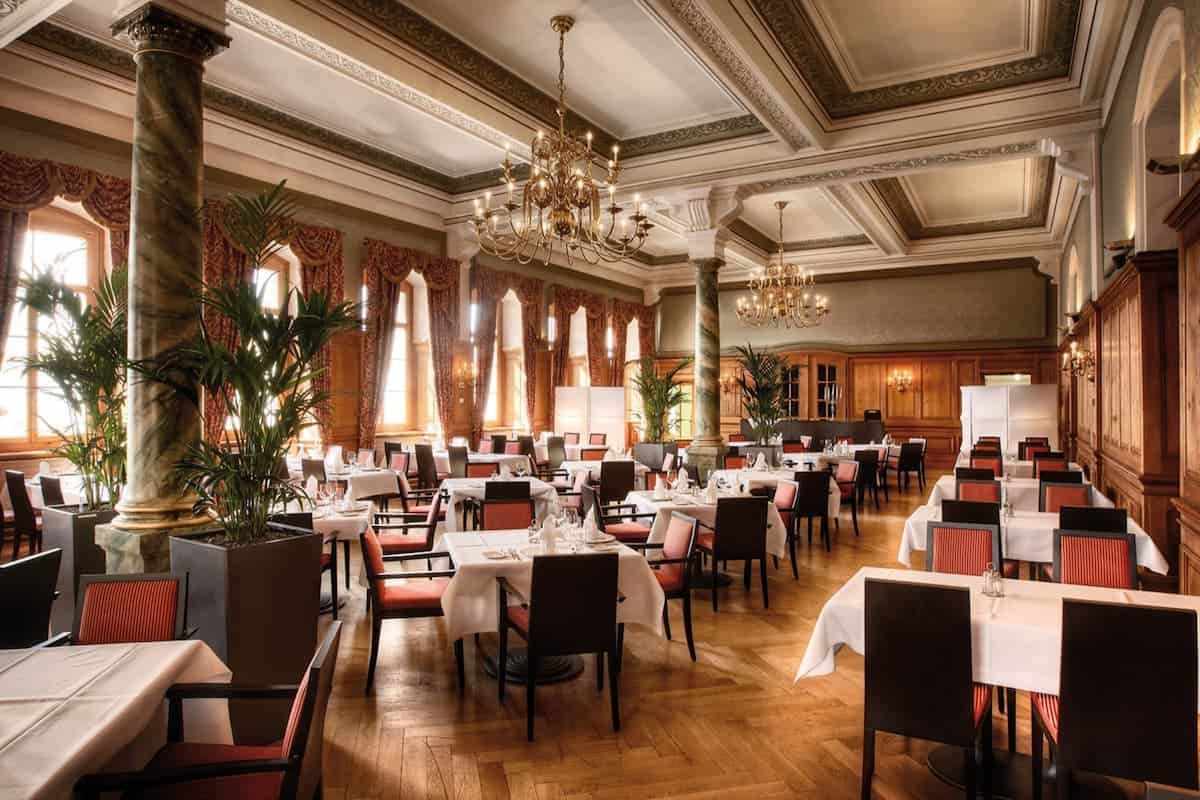 Elegant Queen Victoria Hall restaurant at Hotel Pilatus Kulm, featuring classic Swiss decor, chandeliers, and fine dining tables.